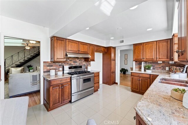 kitchen with brown cabinetry, visible vents, range with two ovens, a sink, and under cabinet range hood