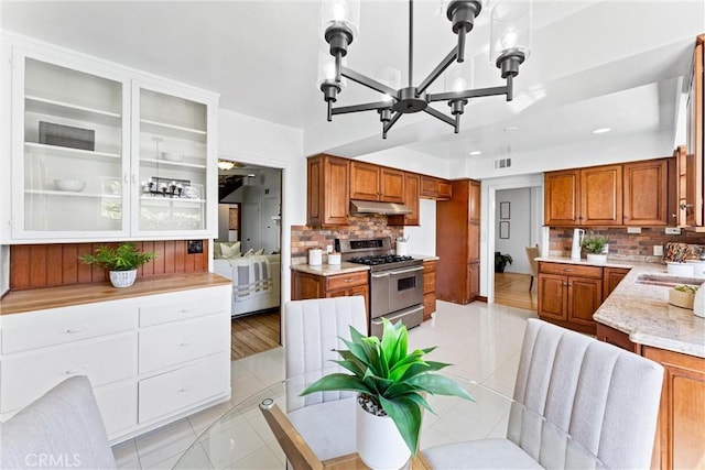 kitchen with an inviting chandelier, brown cabinets, under cabinet range hood, and double oven range