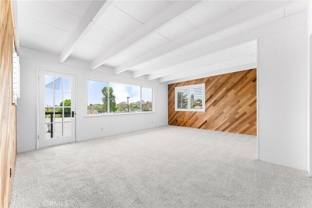 carpeted spare room with wood walls and beam ceiling