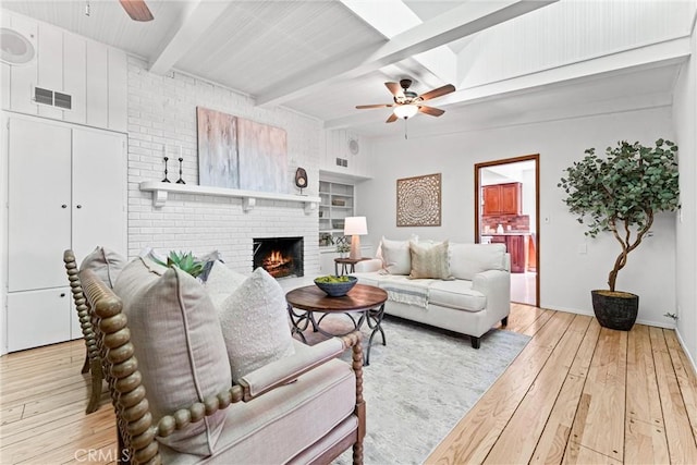 living area featuring wood-type flooring, beam ceiling, a fireplace, baseboards, and ceiling fan