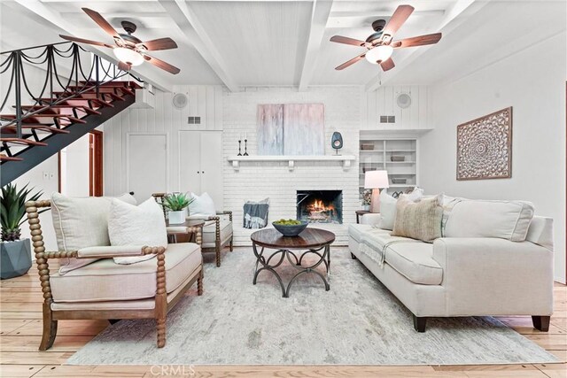 living room featuring beam ceiling, a ceiling fan, wood finished floors, and a brick fireplace