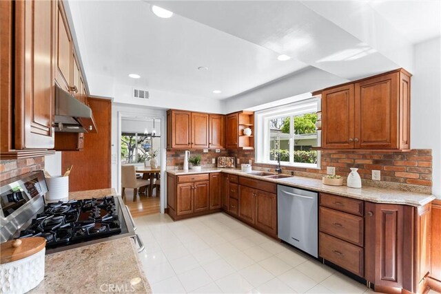 kitchen with range with gas cooktop, brown cabinets, dishwasher, a sink, and under cabinet range hood