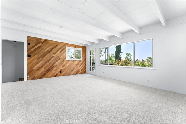 carpeted spare room with beam ceiling and wooden walls