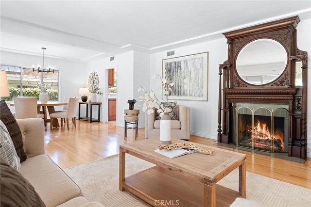 living room with an inviting chandelier, light wood-style floors, visible vents, and a large fireplace
