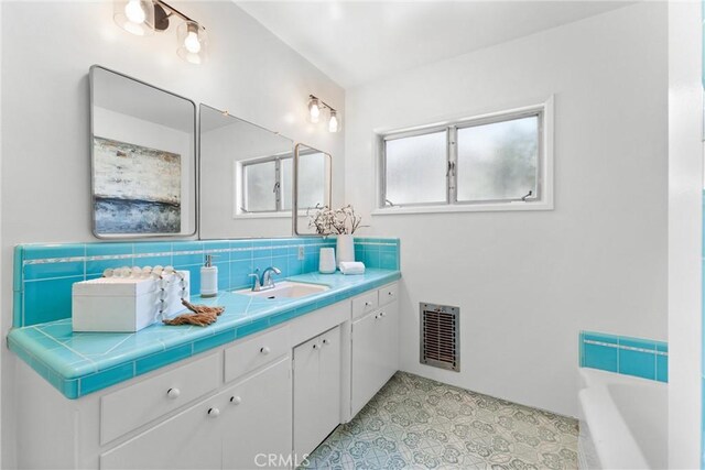 bathroom with visible vents, a tub to relax in, and vanity