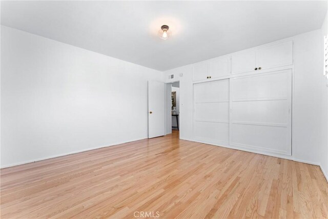 unfurnished bedroom with visible vents, light wood finished floors, and a closet