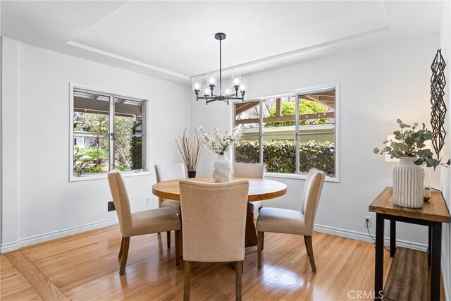 dining space featuring baseboards, a raised ceiling, light wood finished floors, and a notable chandelier