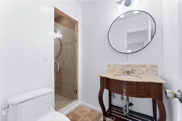 full bath with toilet, baseboards, tasteful backsplash, a sink, and a stall shower