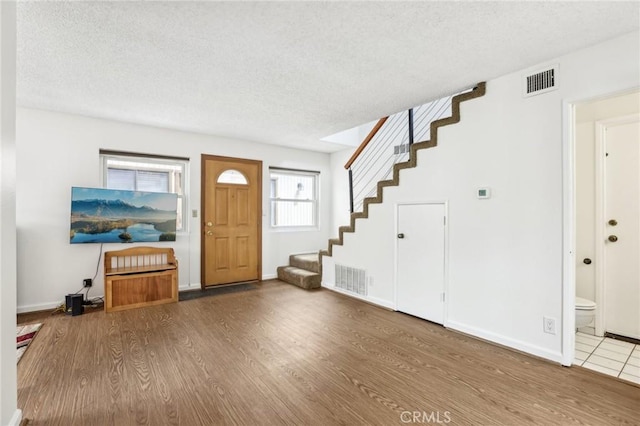 entryway featuring a textured ceiling, stairs, wood finished floors, and visible vents