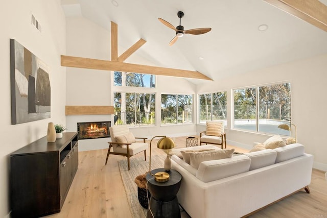 living area featuring visible vents, a glass covered fireplace, ceiling fan, high vaulted ceiling, and light wood finished floors