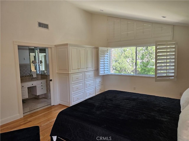 bedroom with visible vents, light wood-style floors, and high vaulted ceiling