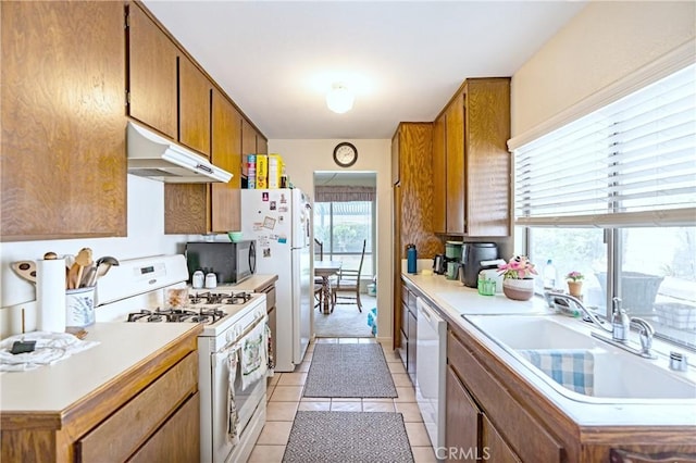 kitchen with under cabinet range hood, brown cabinets, a sink, and white appliances