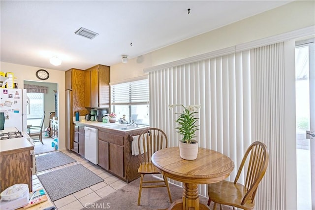 kitchen featuring white appliances, brown cabinetry, a sink, and light countertops