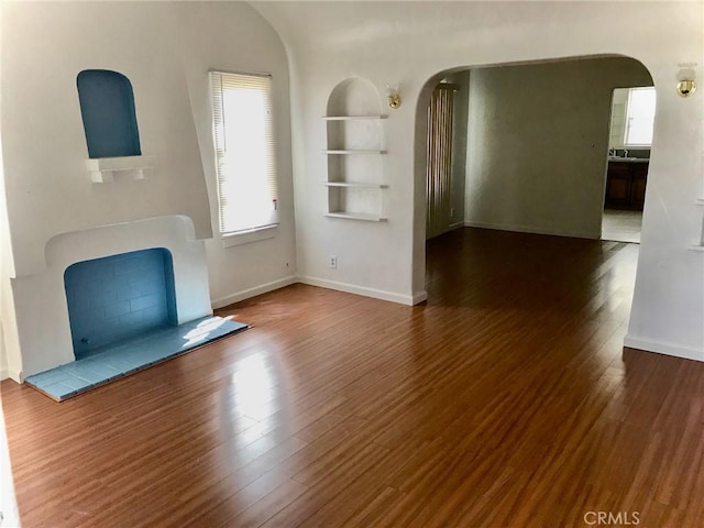 2853 Buckingham Rd, Los Angeles, CA 90016 - unfurnished living room featuring built in features, baseboards, arched walkways, and wood finished floors
