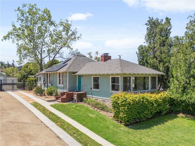 view of front facade with fence, a shingled roof, a front yard, roof mounted solar panels, and a chimney