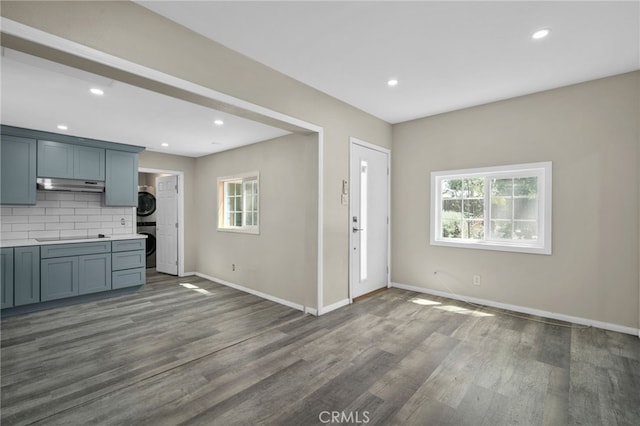 unfurnished living room featuring baseboards, stacked washer / dryer, a wealth of natural light, and dark wood-style floors