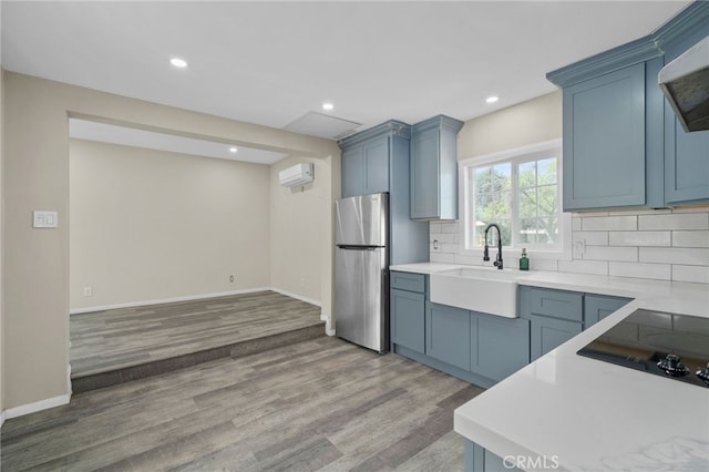 kitchen with freestanding refrigerator, light countertops, a wall unit AC, tasteful backsplash, and a sink