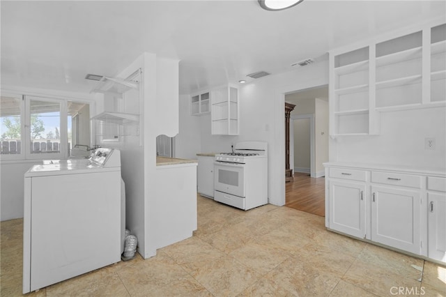 kitchen with white gas stove, washing machine and clothes dryer, visible vents, open shelves, and white cabinetry