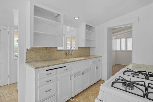 kitchen featuring open shelves, light stone countertops, gas range gas stove, white cabinets, and a sink