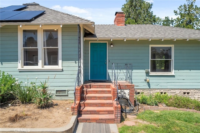 property entrance featuring crawl space, a chimney, roof mounted solar panels, and roof with shingles