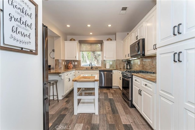 kitchen featuring appliances with stainless steel finishes, a sink, white cabinets, wood counters, and recessed lighting