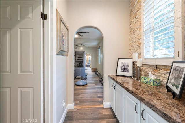 hall featuring baseboards, arched walkways, and dark wood-style floors