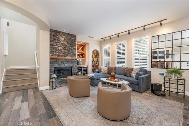 living room with a fireplace, rail lighting, wood finished floors, stairway, and baseboards