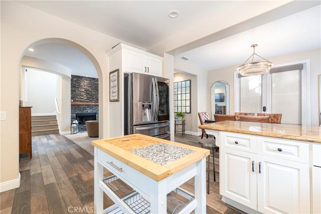 kitchen featuring dark wood-style flooring, a stone fireplace, arched walkways, white cabinets, and stainless steel fridge