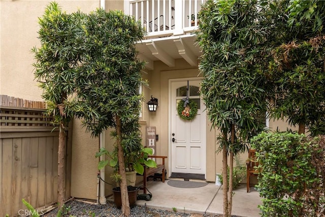 entrance to property featuring fence, stucco siding, and a balcony