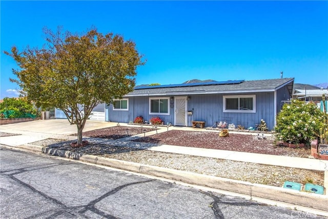single story home featuring an attached garage, concrete driveway, and solar panels