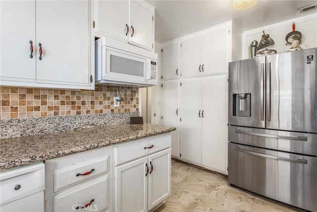 kitchen featuring visible vents, decorative backsplash, white microwave, stainless steel fridge, and white cabinetry