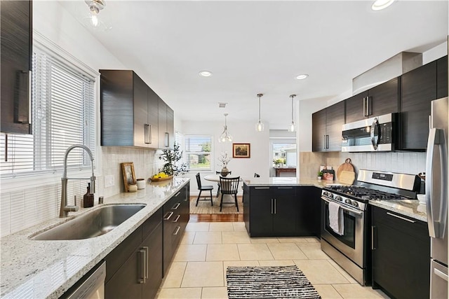 kitchen with tasteful backsplash, a sink, appliances with stainless steel finishes, light tile patterned floors, and hanging light fixtures