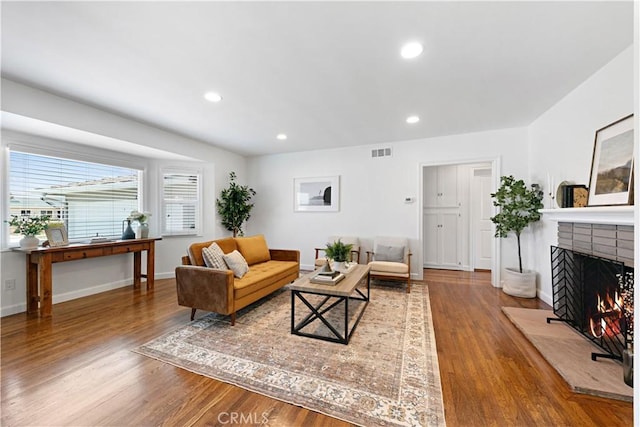 living room with visible vents, wood finished floors, baseboards, a warm lit fireplace, and recessed lighting