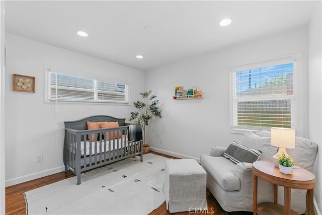 bedroom featuring a nursery area, baseboards, multiple windows, and wood finished floors