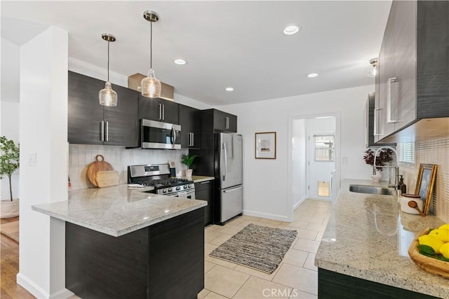 kitchen with a peninsula, tasteful backsplash, dark cabinets, a sink, and stainless steel appliances