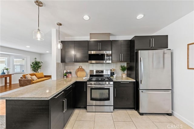 kitchen featuring appliances with stainless steel finishes, hanging light fixtures, dark cabinets, a peninsula, and decorative backsplash