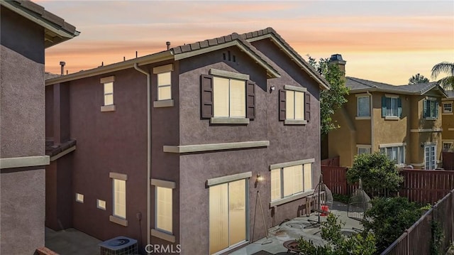 back of house at dusk featuring fence, a patio, and stucco siding