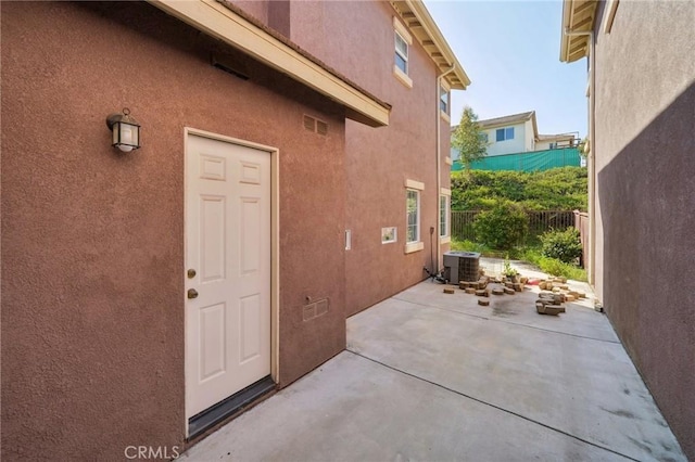 property entrance with fence, central air condition unit, stucco siding, and a patio area