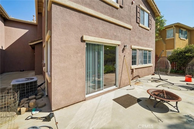 back of property with stucco siding, central AC, a patio area, and an outdoor fire pit