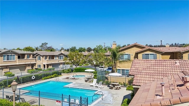 pool with a community hot tub, a patio area, fence, and a residential view