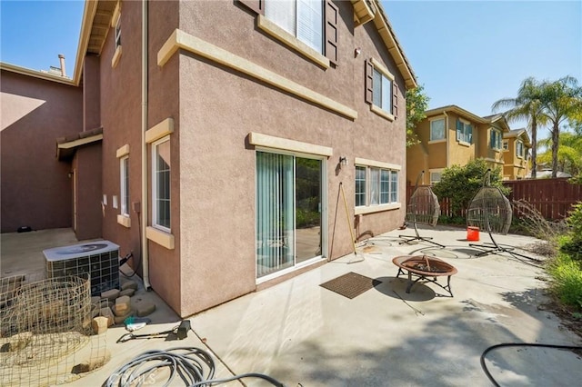back of property featuring fence, stucco siding, cooling unit, a patio area, and a fire pit