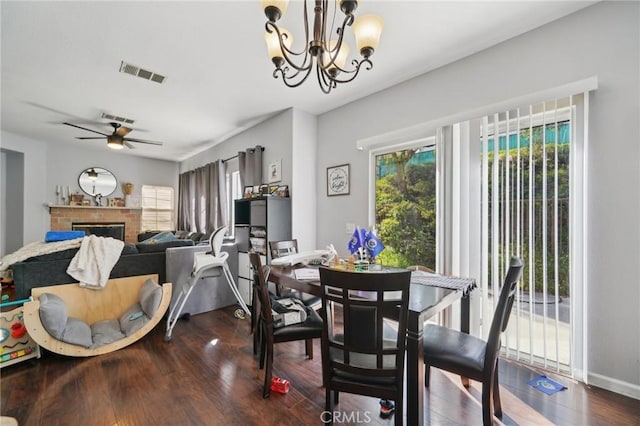 dining space with visible vents, wood finished floors, a fireplace, baseboards, and ceiling fan with notable chandelier
