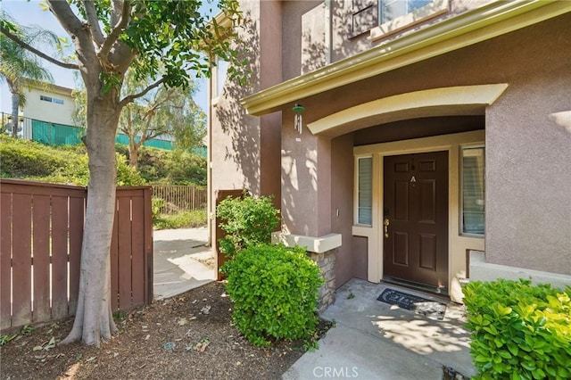 entrance to property featuring fence and stucco siding
