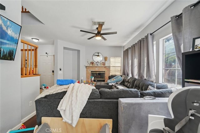 living room with ceiling fan, a brick fireplace, baseboards, wood finished floors, and visible vents
