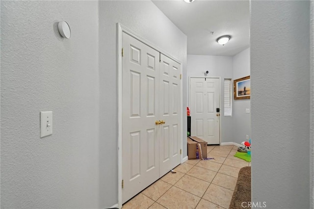 hallway with baseboards, a textured wall, and light tile patterned floors