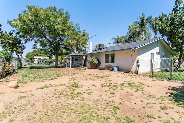 rear view of house featuring fence, central AC, stucco siding, a gate, and a chimney
