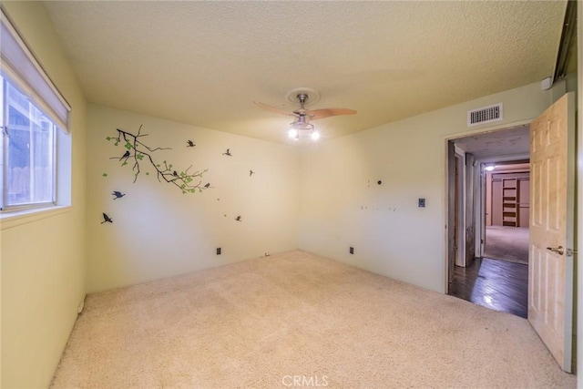 empty room featuring carpet floors, a ceiling fan, a textured ceiling, and visible vents