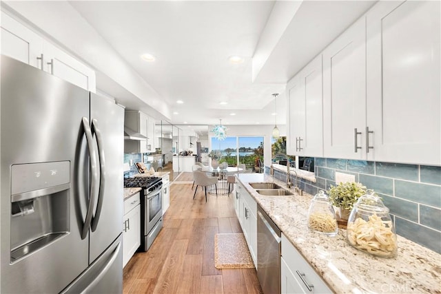 kitchen with a sink, light wood-style floors, stainless steel appliances, white cabinetry, and tasteful backsplash