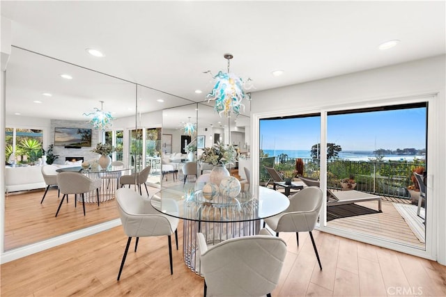 dining room with recessed lighting, light wood finished floors, a water view, and a notable chandelier