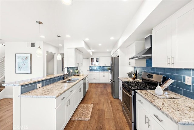 kitchen with a peninsula, wood finished floors, wall chimney exhaust hood, a sink, and appliances with stainless steel finishes